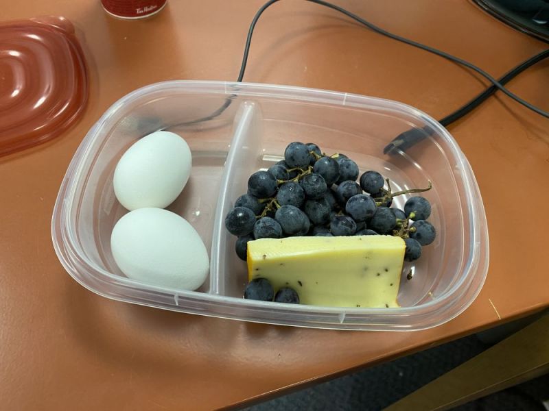 A clear container with a variety of fruits and eggs on a brown surface.