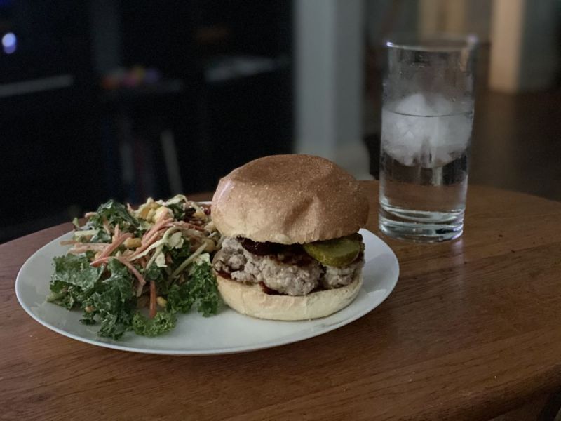 A burger and salad on a white plate next to a glass of water on a wooden surface.