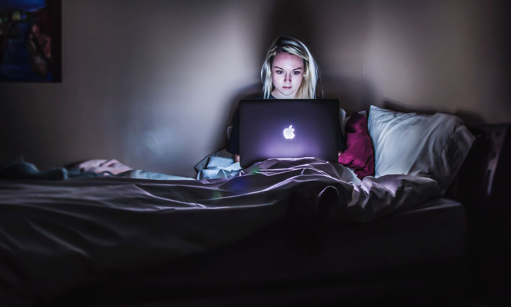 Woman in bed on MacBook in dark room