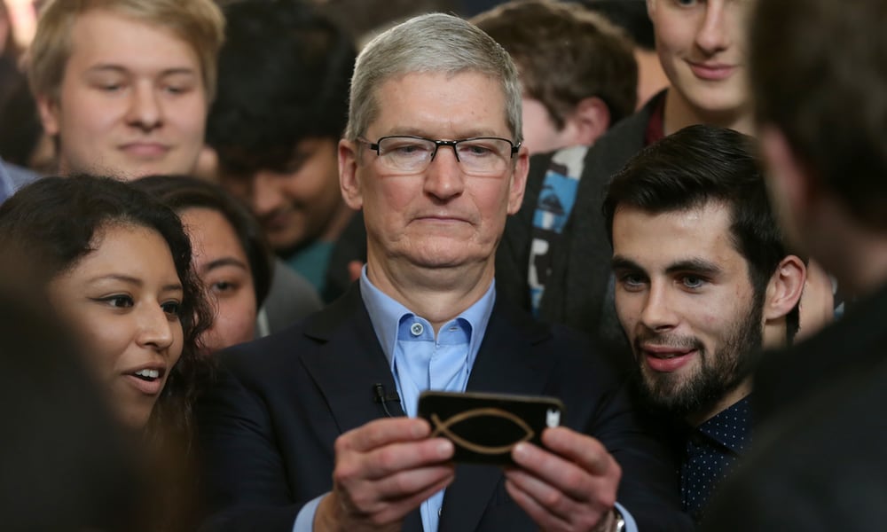 Apple CEO Tim Cook looking at phone taking selfie with students