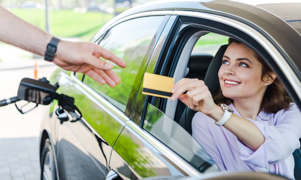 smiling woman handing credit card to gas station attendant