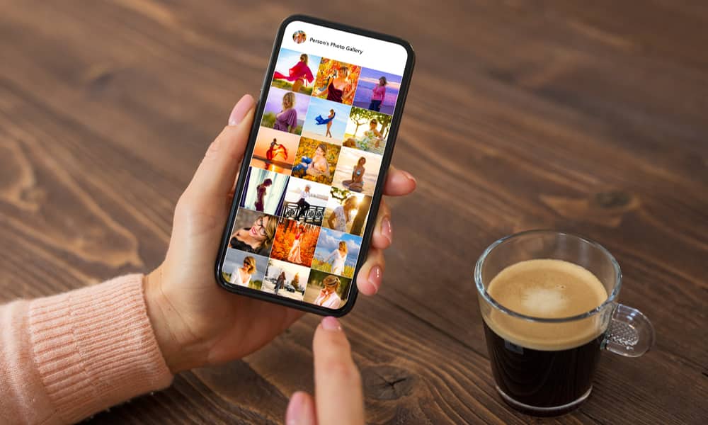 person browsing photos on iPhone over wooden table with coffee