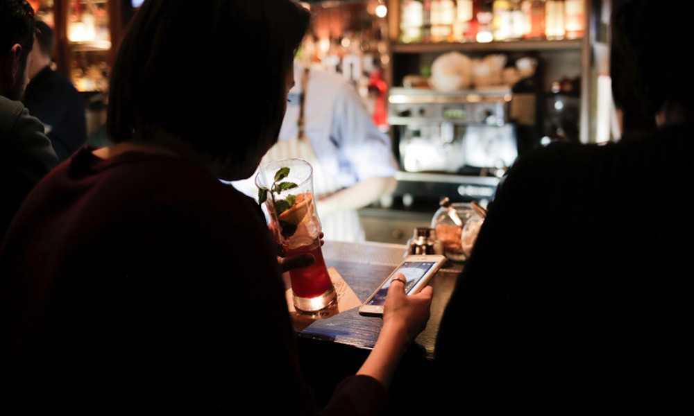 Woman having a drink in a bar and using an iPhone